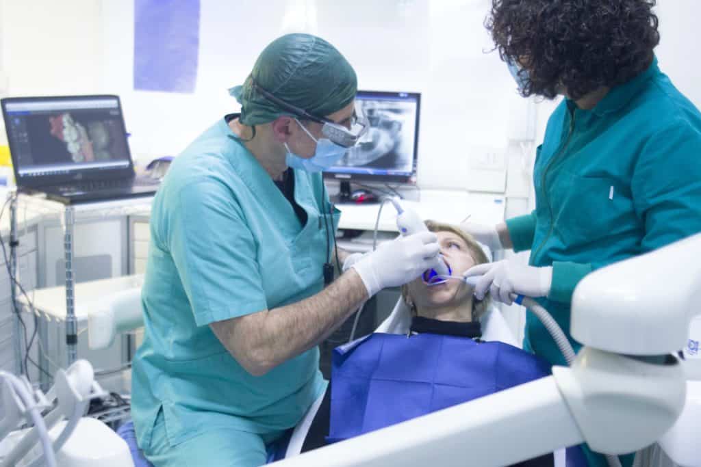 Deep cleaning teeth with two dentists and a patient in the chair.