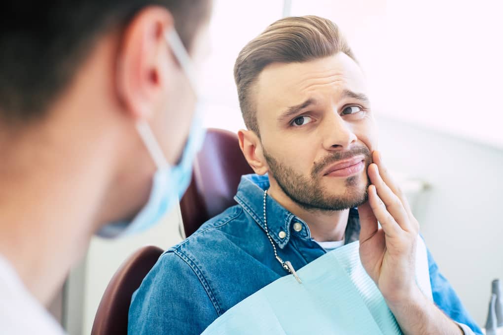 male client sitting in dental chair holding mouth from sinus tooth pain