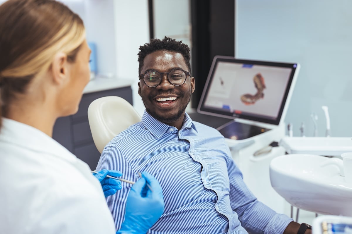 A smiling man sits in a dental chair talking to a dentist