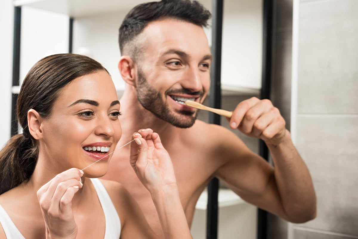 A woman flosses her teeth while a man brushes his teeth