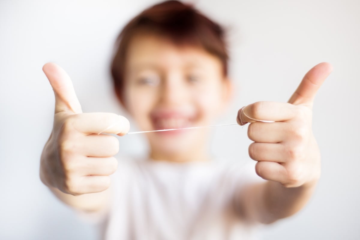 A child smiling and stretching a piece of floss between their thumbs