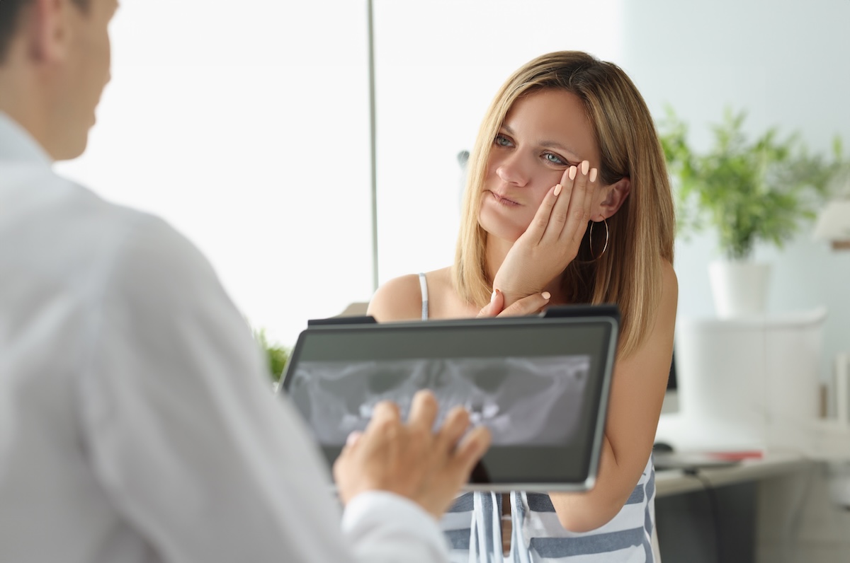 A woman sits in a dental office, touching her cheek in discomfort,