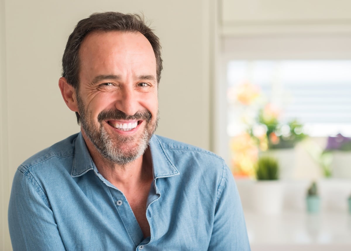 A middle-aged man with a beard and dark hair smiles warmly at the camera